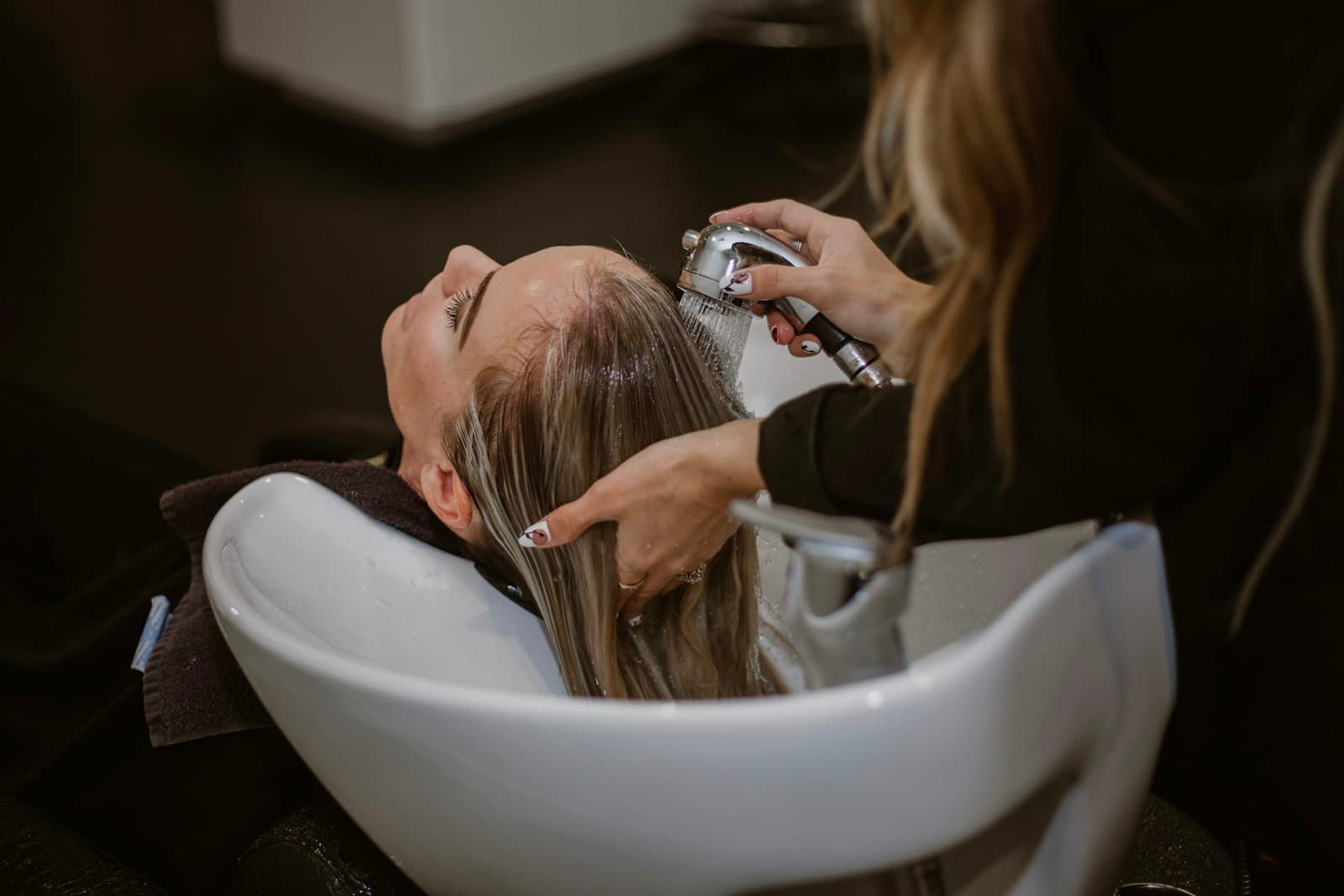Coiffeuse lavant les cheveux d'une cliente au bac du salon